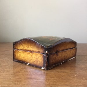 May include: A small wooden box with a domed lid. The box is painted in a dark brown color with a gold-colored pattern. The lid is decorated with a painted scene.