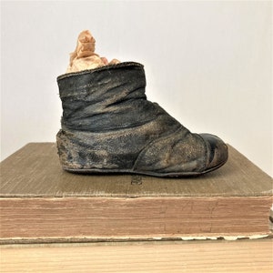May include: A vintage leather baby boot with a worn brown finish. The boot is sitting on top of a stack of books.
