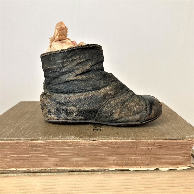 May include: A vintage leather baby boot with a worn brown finish. The boot is sitting on top of a stack of books.