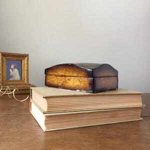 May include: A small, wooden box with a dark brown finish and a light brown marbled pattern. The box is sitting on top of two books.