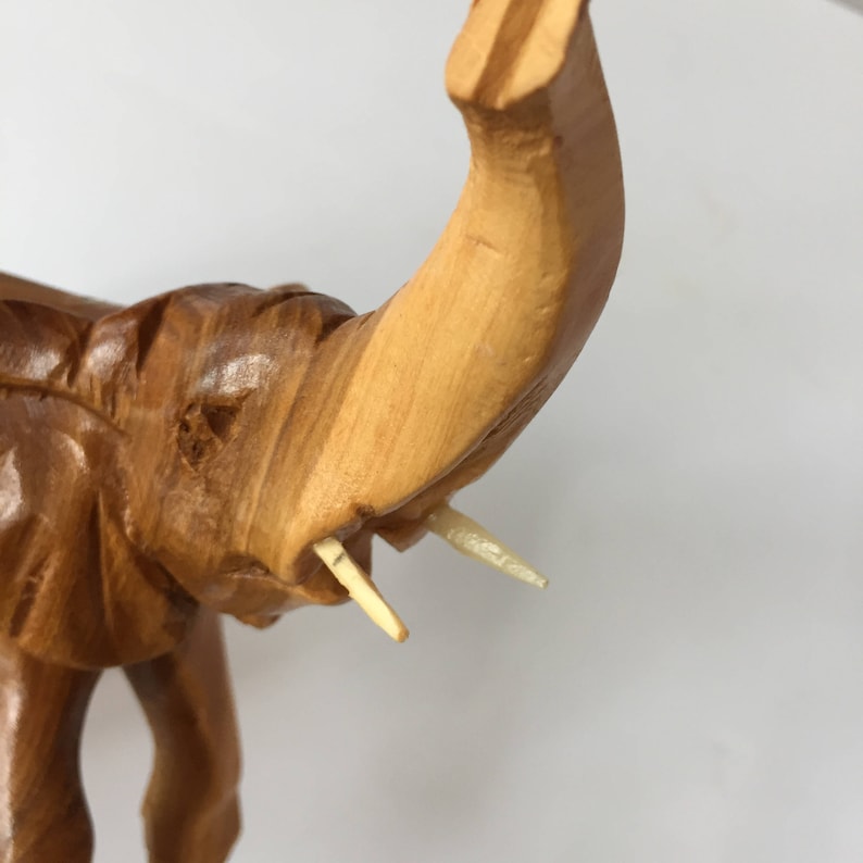 May include: Close-up of a wooden elephant figurine with its trunk raised. The elephant has detailed carving and ivory-coloured tusks.