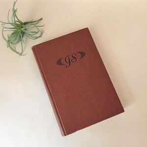May include: A brown hardcover book with the initials "JS" embossed on the front cover.