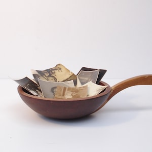 May include: A wooden bowl with a handle, filled with old black and white photographs.