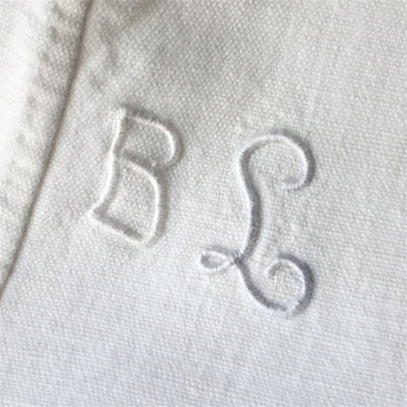 May include: White fabric with embroidered letters "B" and "S" in a cursive font.