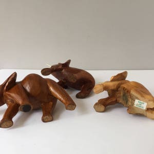 May include: Three wooden elephant figurines, carved in a dark brown colour. The elephants are in different poses, and one has a label that reads "Made in Kenya".
