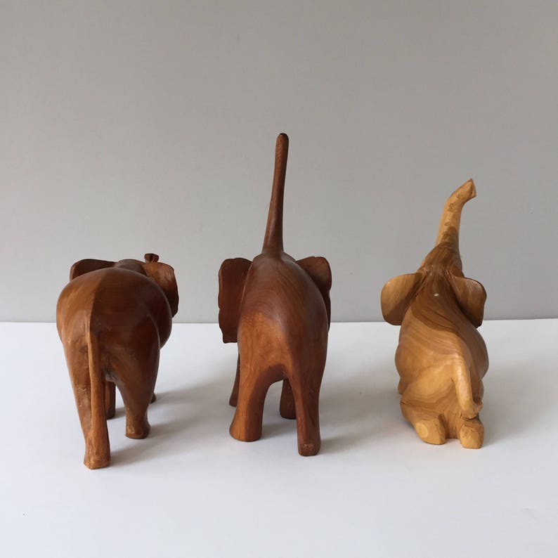 May include: Three wooden elephant figurines, each carved in a different pose. The elephants are all brown and have a natural wood finish.