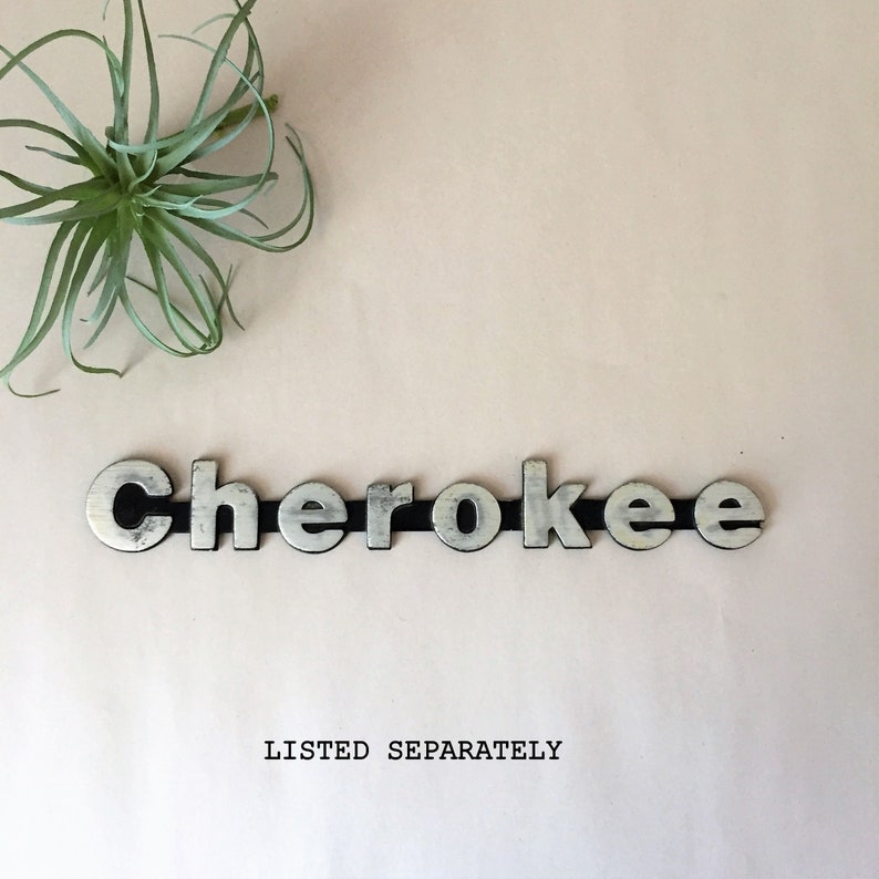 May include: Silver metal letters spelling out the word "Cherokee" on a light pink background. The letters are separated by a black strip.