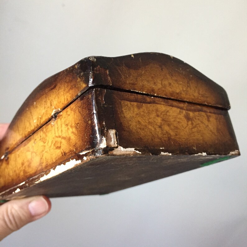 May include: A wooden box with a brown, distressed finish. The box has a slightly curved top and a hinged lid. The box is slightly worn and has some paint chips.