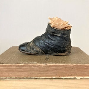 May include: A black leather baby shoe with a worn appearance. The shoe is sitting on top of a stack of books.