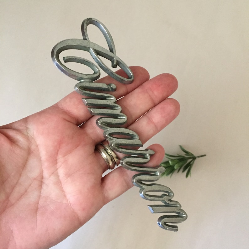 May include: Silver-colored metal emblem with the word "Immaculate" written in a stylized script font.