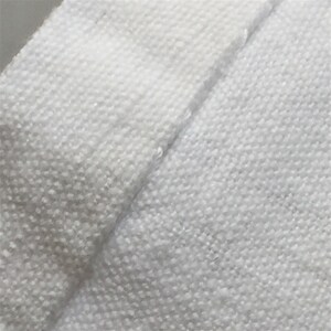 May include: Close-up of a white fabric with a textured weave. The fabric is folded over itself, showing the seam.