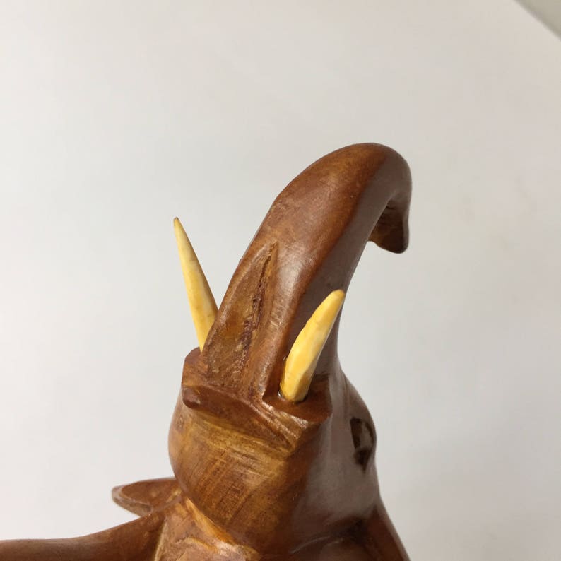 May include: A wooden elephant figurine with a raised trunk and two ivory tusks. The elephant is carved in a light brown colour and has a detailed texture.