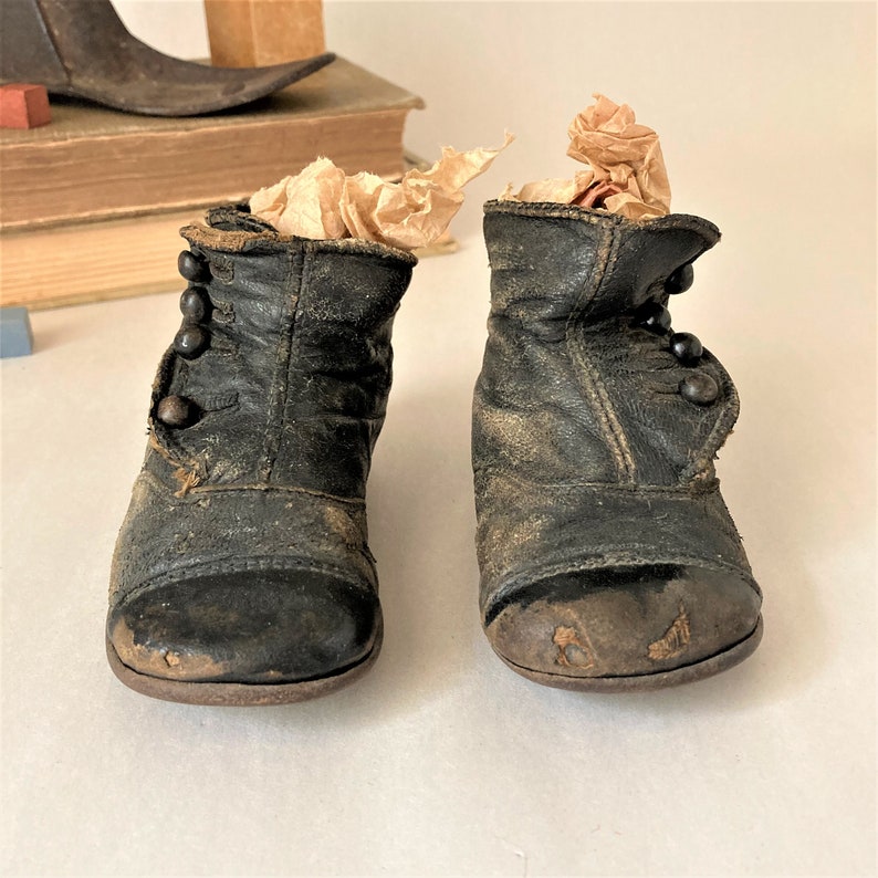 May include: A pair of black leather baby boots with button closures. The boots are worn and have a distressed look.