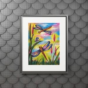 Könnte beinhalten: Ein gerahmtes Gemälde mit zwei Libellen mit blauen und violetten Flügeln, die über grünem Gras und rosa Blütenknospen vor einem leuchtend gelben, orangen und blauen Himmel fliegen. Das Kunstwerk befindet sich in einem schwarzen Rahmen mit weißem Passepartout.