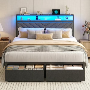 May include: A dark gray upholstered bed frame featuring a headboard with integrated blue LED lighting, open shelving, and two large pull-out storage drawers at the base. The bed is dressed with white linens, a beige throw, and several decorative pillows.
