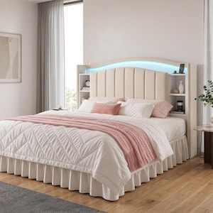 May include: A beige upholstered bed frame with a vertical channel-tufted headboard, integrated side shelving, and built-in blue LED lighting. The bed is dressed in white quilted bedding with a pink throw blanket and a white ruffled bed skirt.