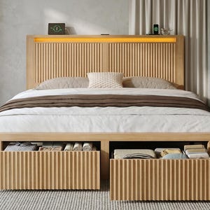 May include: A light wood bed frame featuring a headboard with vertical slats and integrated warm LED lighting. The base includes two large pull-out storage drawers with matching vertical slat fronts, filled with folded textiles and clothing items.