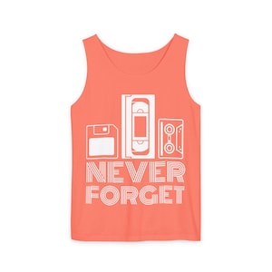 May include: A coral-colored tank top featuring a white graphic print of a floppy disk, a VHS tape, and a cassette tape above the text NEVER FORGET. The design is centered on the front of the garment, which has a scoop neckline and sleeveless cut.
