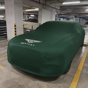 以下が含まれることがあります： ダークグリーンのカーカバーが車両を覆っており、ボンネット部分には白いベントレーのロゴと「BENTLEY」の文字がプリントされています。生地は滑らかで体にフィットし、車体やその下の細部を完全に隠しています。