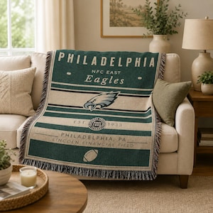 Könnte beinhalten: Eine gewebte Wohndecke mit Philadelphia Eagles Branding in Dunkelgrün und Creme. Das Design zeigt den Teamnamen, das Logo, das Gründungsjahr 1933, den Schriftzug Lincoln Financial Field und eine Football-Grafik mit Fransen an den Seiten.