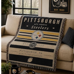 Könnte beinhalten: Eine gewebte Wohndecke mit dem Logo der Pittsburgh Steelers, dem Teamnamen und Texten wie Est. 1933, Pittsburgh, PA und Acrisure Stadium. Das Design zeigt schwarze, goldene und cremefarbene Streifen mit einer Football-Grafik und gefransten Kanten.