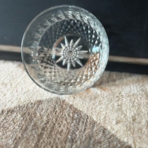 May include: A clear glass bowl featuring a detailed diamond-cut pattern across its exterior surface and a prominent, multi-pointed starburst design etched into the center of the base, creating a reflective and textured appearance throughout.