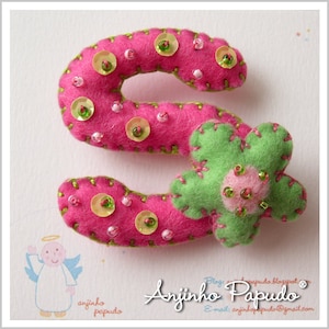 May include: A pink felt letter S with green stitching and a green felt flower with pink beads. The letter is decorated with pink and green sequins.