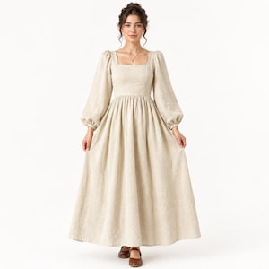 Op de afbeelding: Een beige jurk tot op de grond met lange, volumineuze mouwen die bij de manchetten zijn geplooid. Het kledingstuk heeft een vierkante halslijn, een aansluitend lijfje en een volle, zwierige rok die tot op de grond reikt.