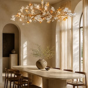 May include: A gold branch-style chandelier featuring numerous translucent clear and amber-colored glass flower blossoms. The fixture is suspended from a central gold rod and illuminates the space with a warm, organic, and branching design.