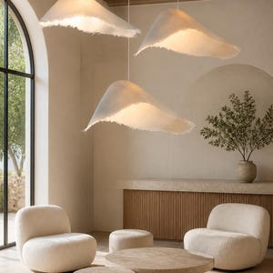 May include: Three off-white pendant lights with irregular, organic, wave-like shapes and frayed, textured edges. Each light is suspended by a thin white cord from the ceiling, emitting a soft, warm glow that illuminates the space below.
