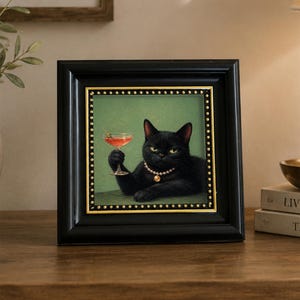 Può includere: Un'opera d'arte da parete incorniciata raffigurante un gatto nero che indossa una collana di perle e tiene in mano un bicchiere da martini con un'oliva. L'illustrazione è su sfondo verde unito, in una cornice nera con borchie decorative dorate.