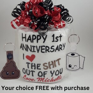 May include: A novelty gift set for a 1st anniversary. It includes a roll of toilet paper with the text "Happy 1st Anniversary" and a humorous message. The gift is decorated with red and black ribbons and includes a keychain.