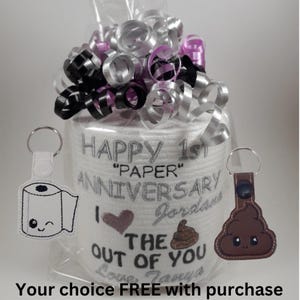 May include: A novelty gift set featuring a roll of toilet paper with embroidered text reading "Happy 1st Anniversary" and "I love the crap out of you." Includes a keychain with a smiling poop emoji and a keychain with a smiling toilet paper roll.