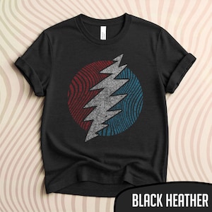 May include: Black heather t-shirt featuring a circular design with a lightning bolt graphic. The design is split into red and blue sections with a gray lightning bolt in the center. The shirt has rolled-up sleeves.