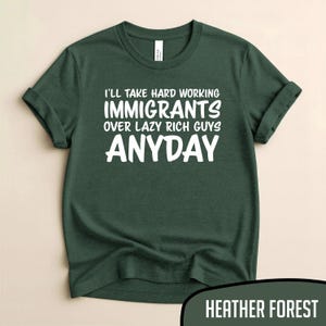 Puede incluir: Una camiseta verde oscuro con las mangas enrolladas. La camiseta presenta texto blanco que dice: "I'LL TAKE HARD WORKING IMMIGRANTS OVER LAZY RICH GUYS ANYDAY." La esquina inferior derecha de la imagen tiene el texto "HEATHER FOREST".