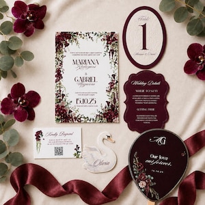 Pode incluir: Um conjunto de papelaria de casamento com um convite retangular, um cartão de número de mesa, um cartão de detalhes, um marcador de lugar em forma de cisne com o nome Olivia e um cartão de resposta com código QR e flores bordô.