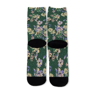 May include: A pair of crew socks featuring a dark green background with a repeating floral pattern in shades of light purple, cream, and dark green, finished with solid black heels and toes for a distinct contrast in the design.