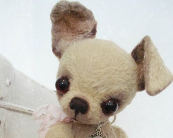 May include: A beige plush toy chihuahua with brown ears and a locket necklace. The locket has a picture of a couple inside.
