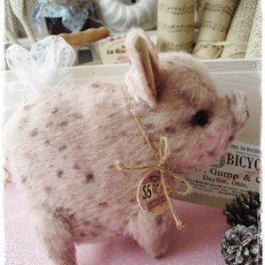 May include: A small, pink pig with brown spots is sitting on a pink surface. The pig has a brown string tied around its neck with a price tag that says "$5 TABASCO SA".