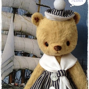 Peut inclure: Un ours en peluche habillé en marin avec un chapeau de marin blanc, un col blanc et une robe rayée bleu et blanc. L'ours regarde un voilier en arrière-plan. La bulle de pensée au-dessus de l'ours dit "Ahoy !"