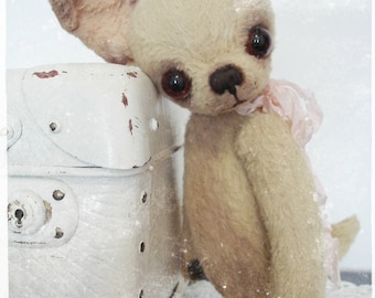 May include: A beige plush toy dog with floppy ears, brown eyes, and a pink ribbon around its neck. The dog is standing next to a white suitcase.