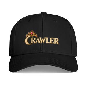 May include: A black baseball cap featuring the word CRAWLER embroidered in a gold serif font across the front. Above the letter C, a gold crown design is detailed with a small red gemstone, creating a distinct graphic element on the cap.