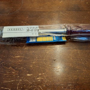 May include: A Vessel brand torque screwdriver with a dark red handle and a silver metal shaft, enclosed in a clear plastic sleeve. A white label with the text VESSEL and Japanese characters is attached to the shaft, along with a blue and yellow insert.