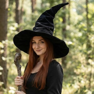 May include: A tall, pointed black witch hat with a wide, flexible brim, paired with a simple black dress and a rustic, gnarled wooden staff. The hat features a soft, textured fabric that curves slightly at the top, creating a classic silhouette.