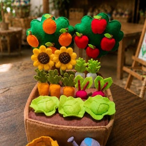 May include: A felt garden playset featuring a brown rectangular planter box filled with various soft fabric vegetables and fruits. Included are orange trees, apple trees, sunflowers, carrots, radishes, and lettuce heads, plus a small watering can.