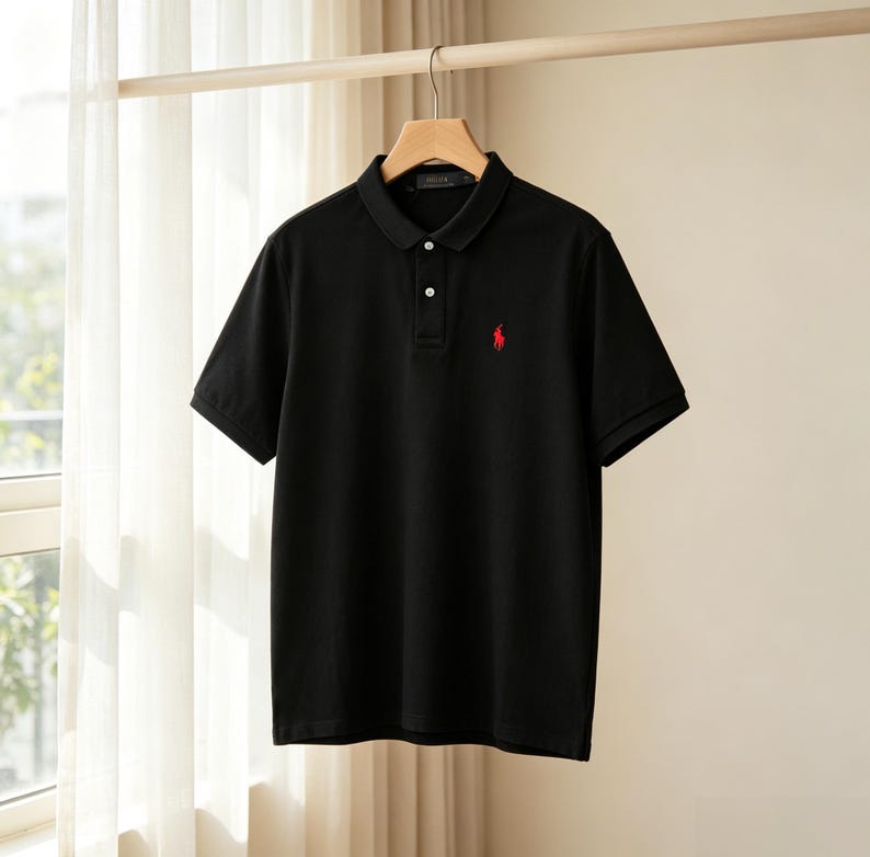 May include: A black short-sleeved polo shirt featuring a classic collar, a two-button placket, and a small red embroidered logo of a person on a horse playing polo on the left chest. The shirt is displayed hanging on a wooden hanger.
