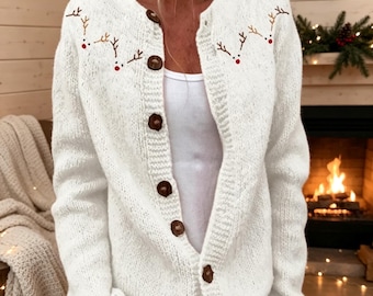 May include: A white long-sleeve knit cardigan featuring a button-down front with dark brown wooden buttons. The upper chest area is decorated with embroidered brown reindeer antlers and small red noses on both the left and right sides.
