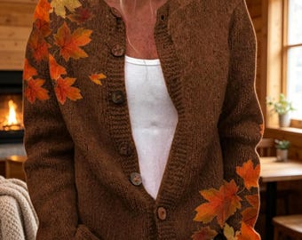 May include: A brown knit cardigan featuring a button-down front and a printed pattern of orange, yellow, and red maple leaves concentrated on the upper right shoulder and the lower left side of the garment, worn over a white top.