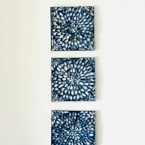 May include: Three square canvases with a blue and white abstract design. The design is made up of small, rounded shapes that are arranged in a circular pattern.