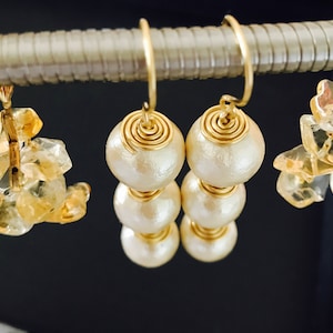 May include: A pair of gold earrings with three white pearl-like beads on each earring. The beads are wrapped in gold wire.